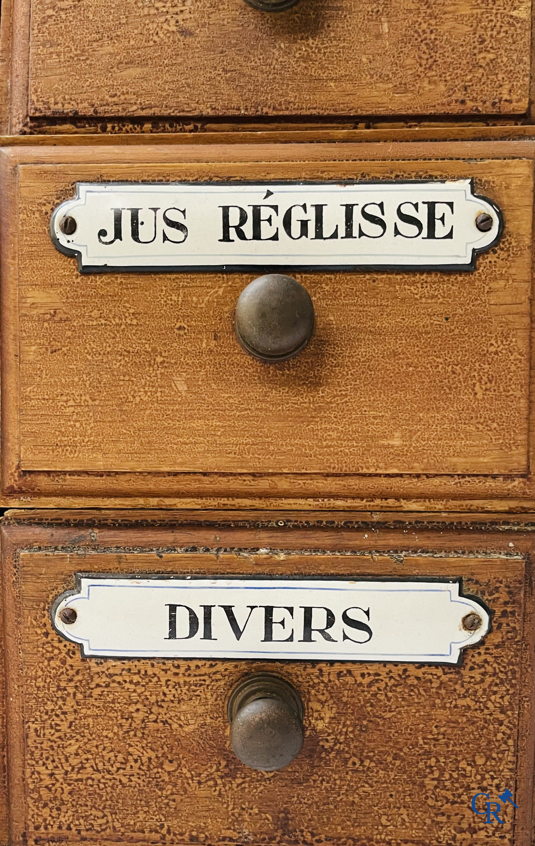 14 laden met emaille bordjes voor kruiden, specerijen en andere afkomstig van een winkelmeubel. Circa 1920.