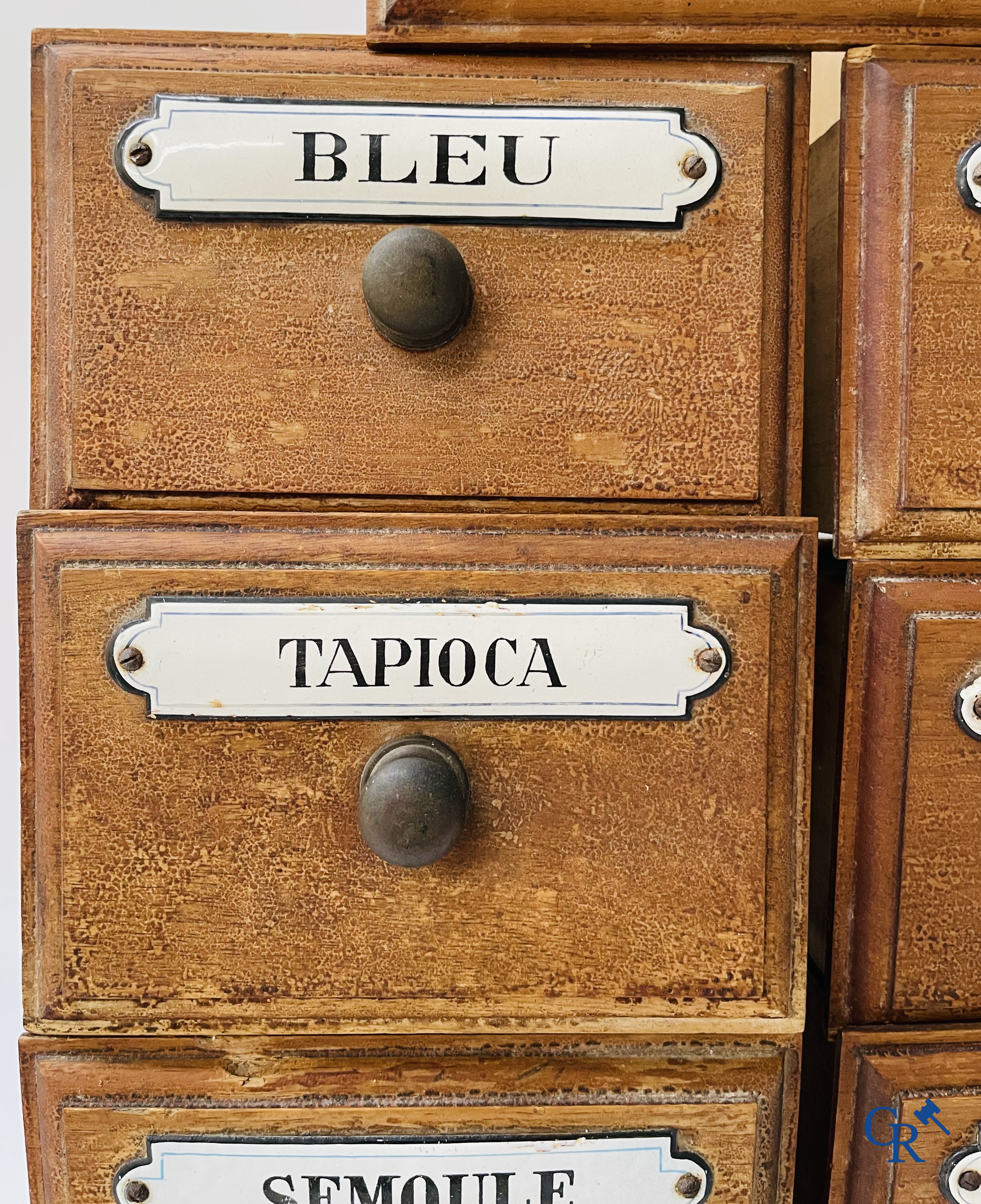 14 laden met emaille bordjes voor kruiden, specerijen en andere afkomstig van een winkelmeubel. Circa 1920.