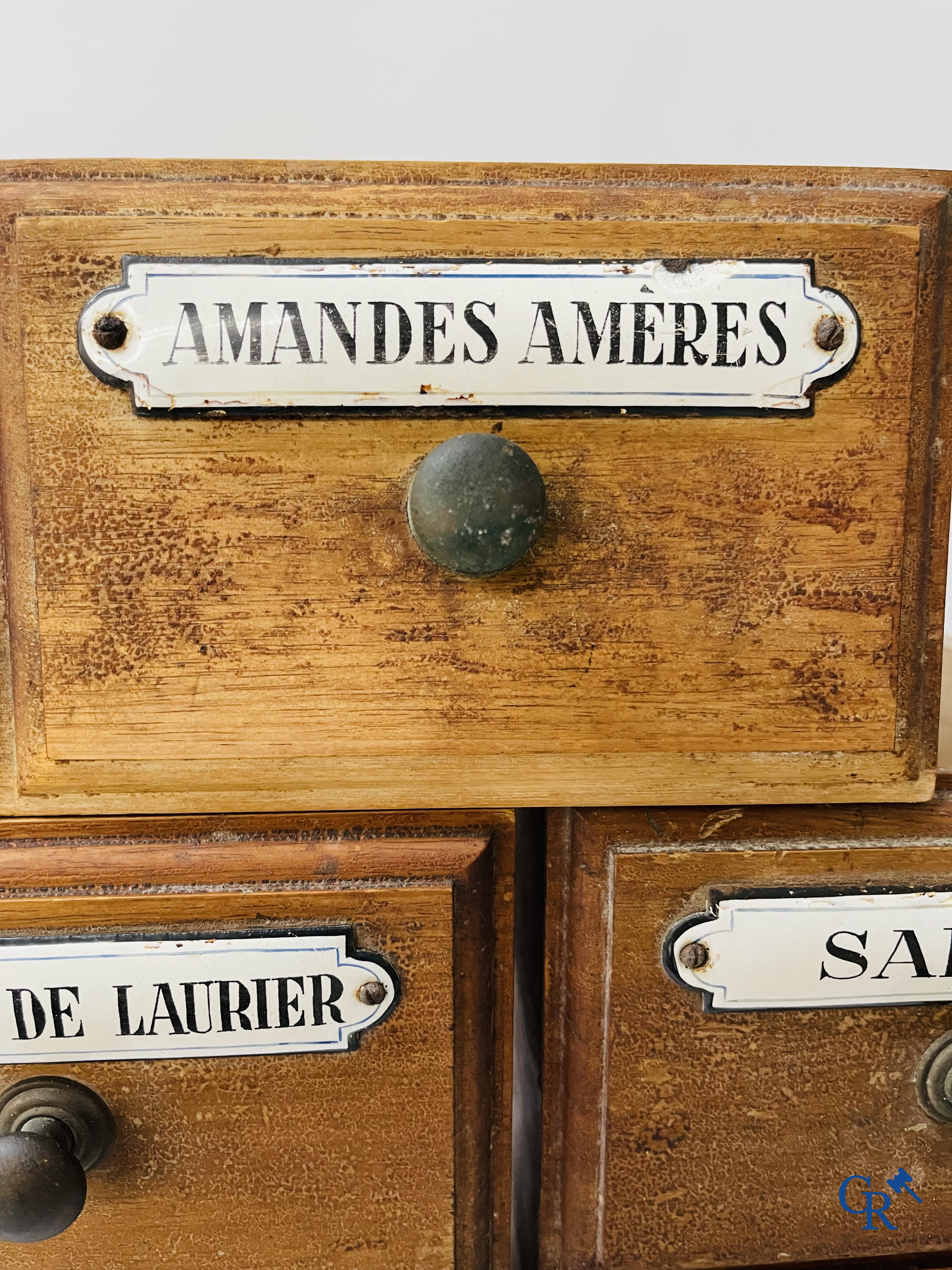 14 laden met emaille bordjes voor kruiden, specerijen en andere afkomstig van een winkelmeubel. Circa 1920.