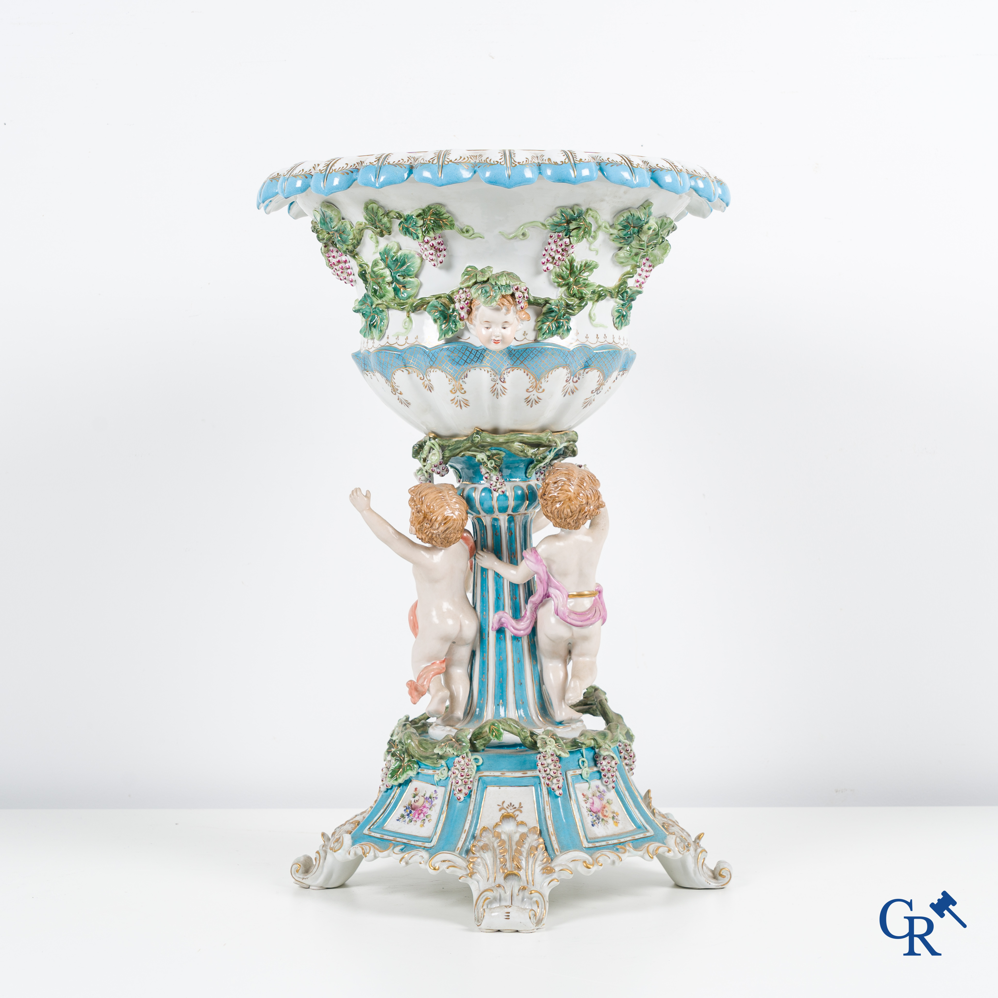 Een grote pronkcoupe in porselein met putti, druivenranken en bacchus hoofden. 20ste eeuw.