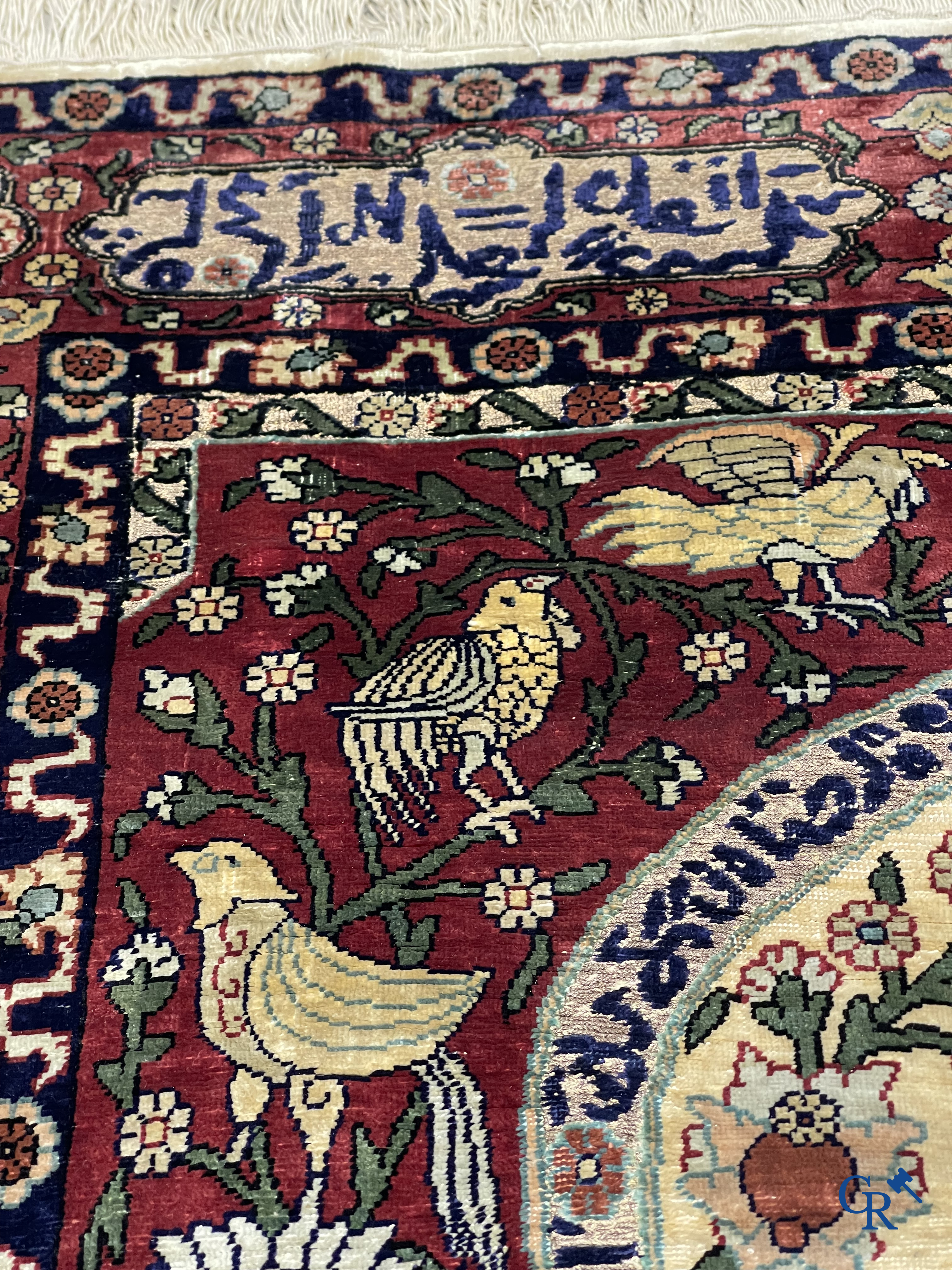 Oosterse tapijten. Een zijden gesigneerd tapijt op donkerrode achtergrond. Inscripties en bewerkt met gouddraad.