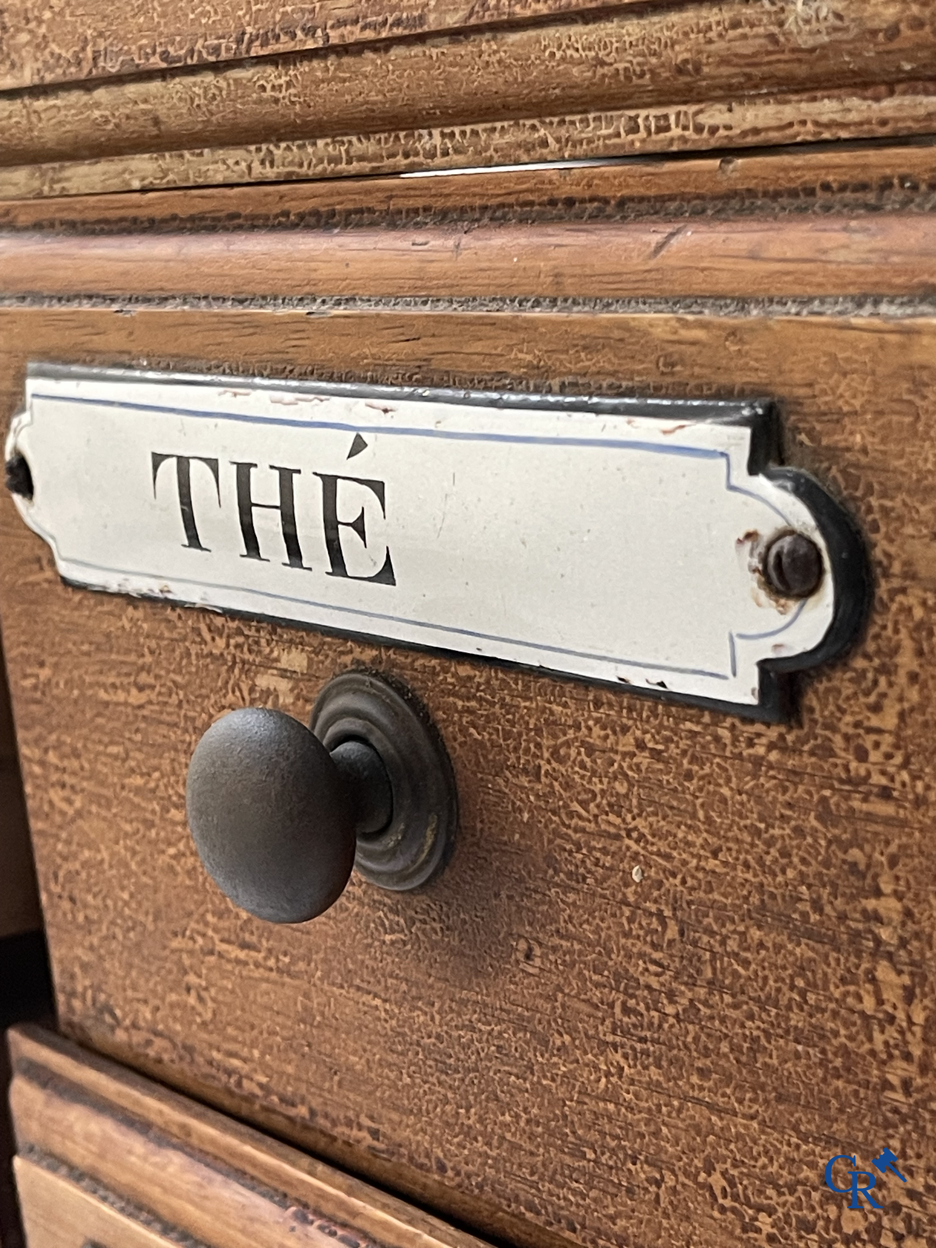 14 laden met emaille bordjes voor kruiden, specerijen en andere afkomstig van een winkelmeubel. Circa 1920.