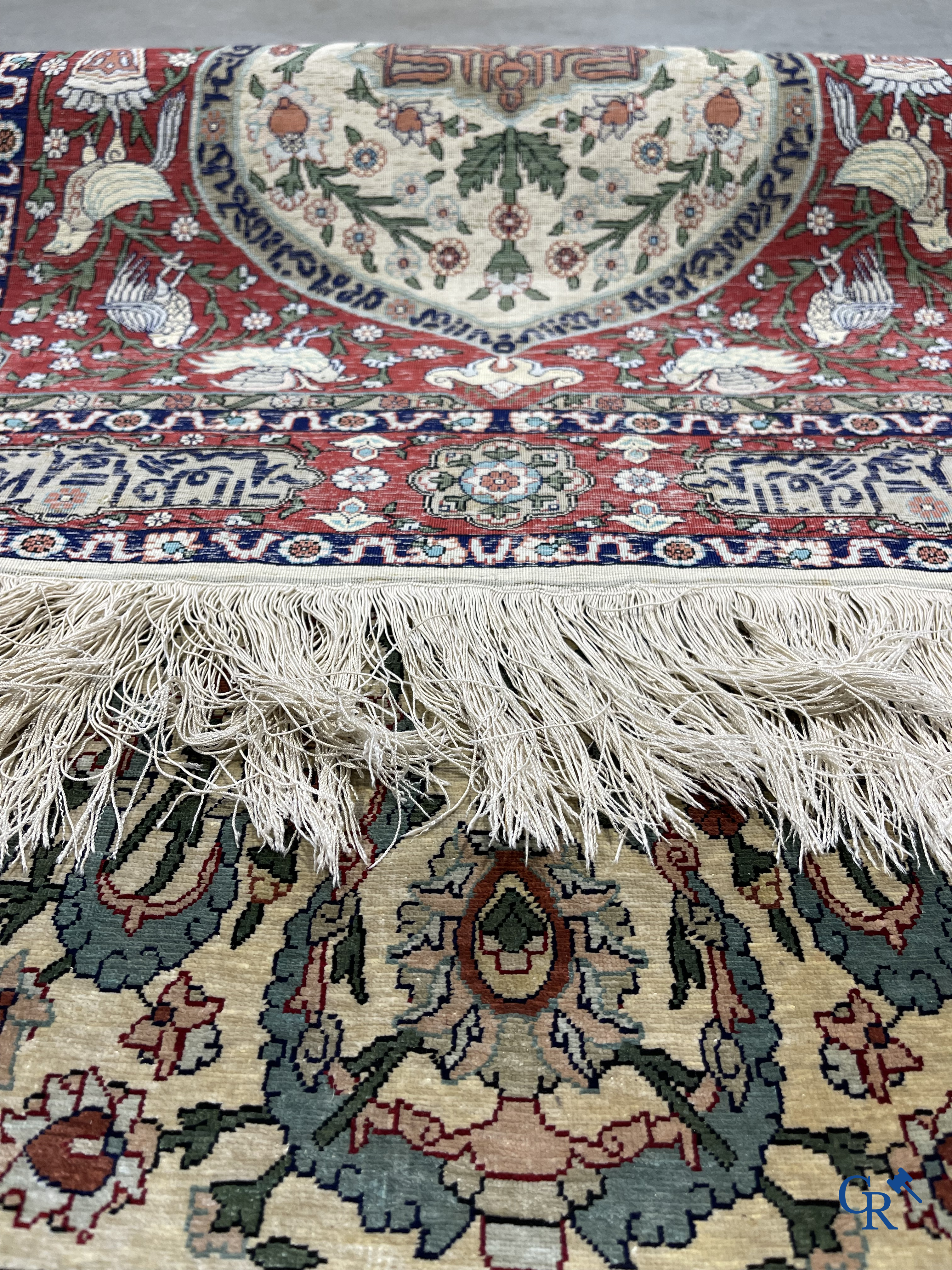 Oosterse tapijten. Een zijden gesigneerd tapijt op donkerrode achtergrond. Inscripties en bewerkt met gouddraad.