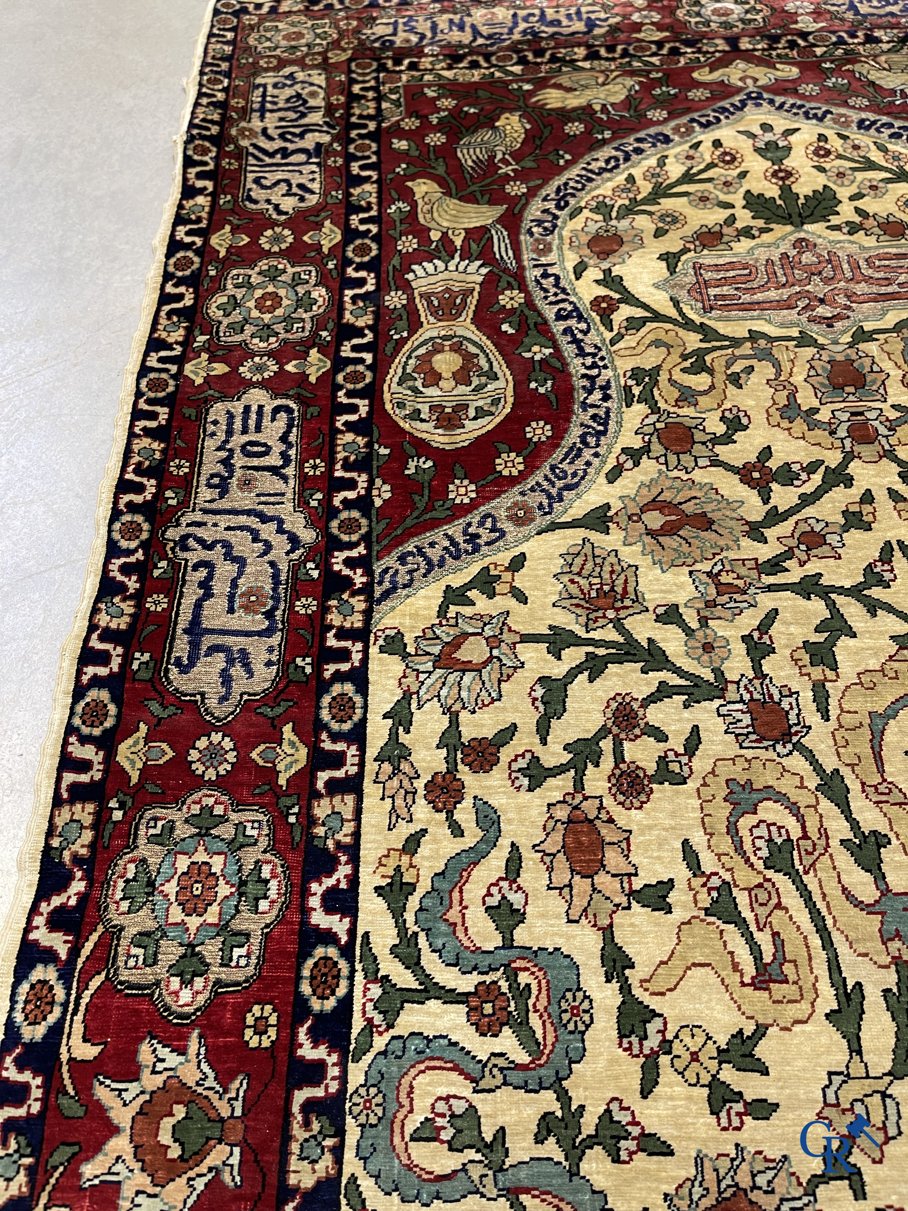 Oosterse tapijten. Een zijden gesigneerd tapijt op donkerrode achtergrond. Inscripties en bewerkt met gouddraad.