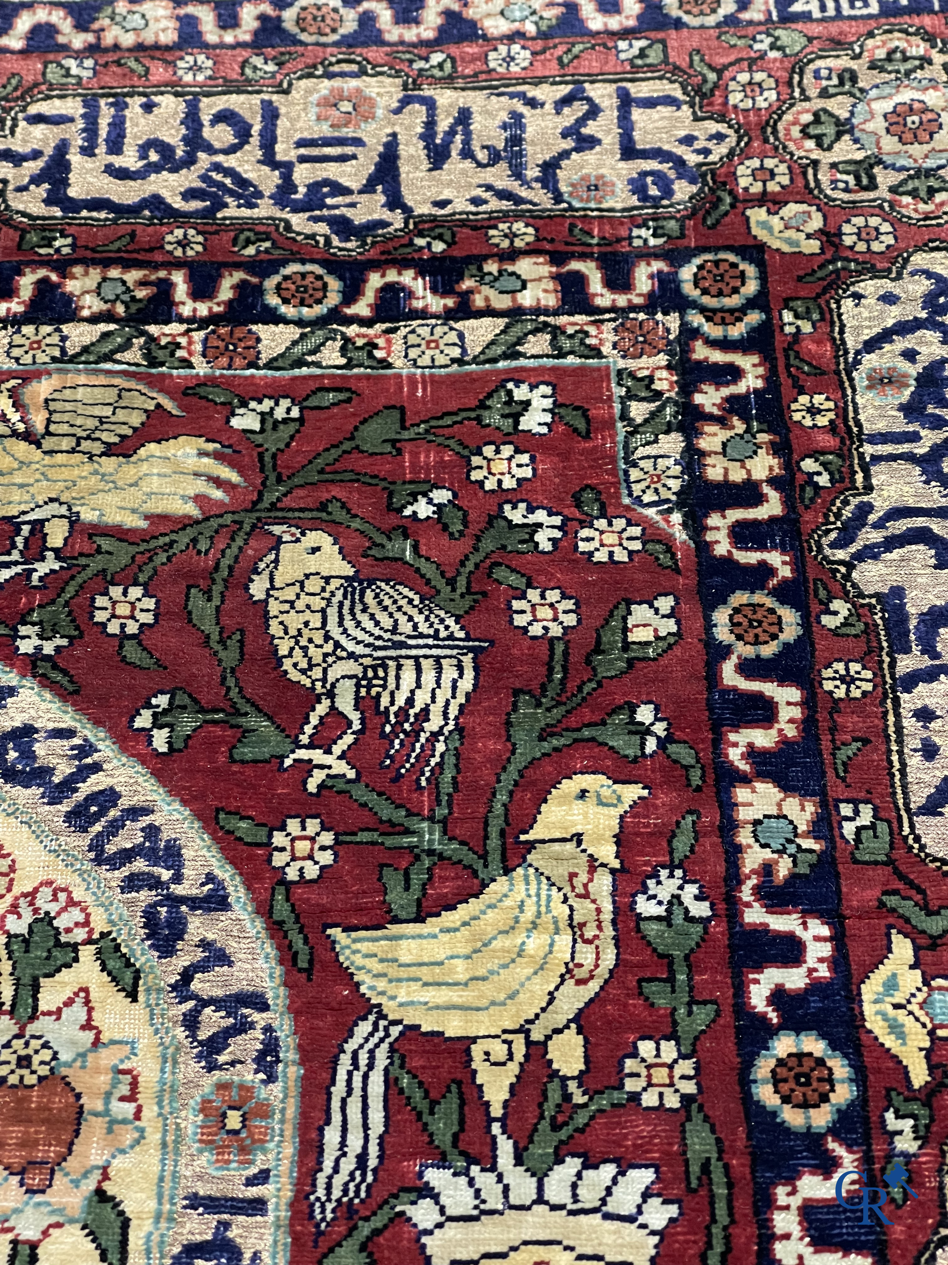 Oosterse tapijten. Een zijden gesigneerd tapijt op donkerrode achtergrond. Inscripties en bewerkt met gouddraad.