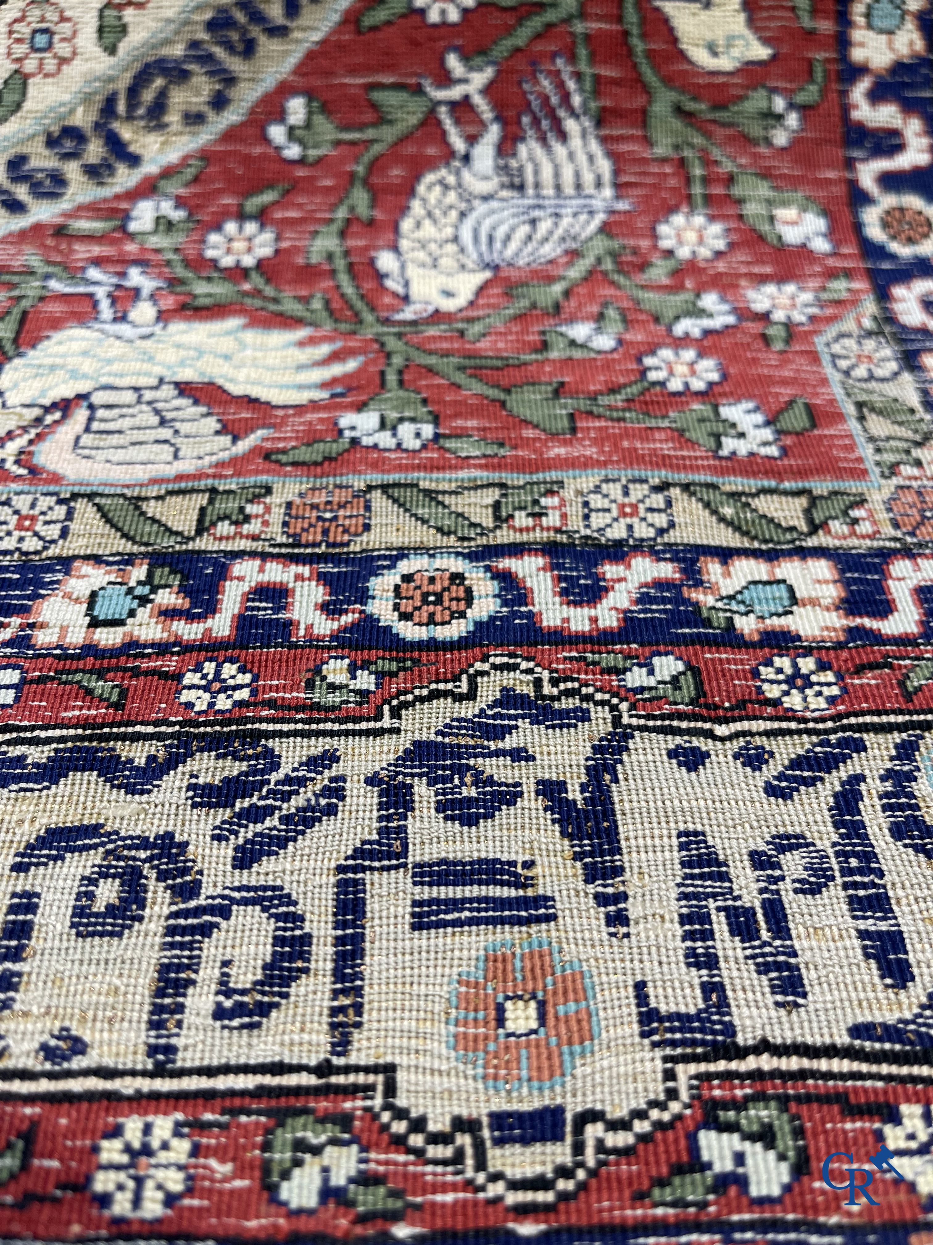 Oosterse tapijten. Een zijden gesigneerd tapijt op donkerrode achtergrond. Inscripties en bewerkt met gouddraad.