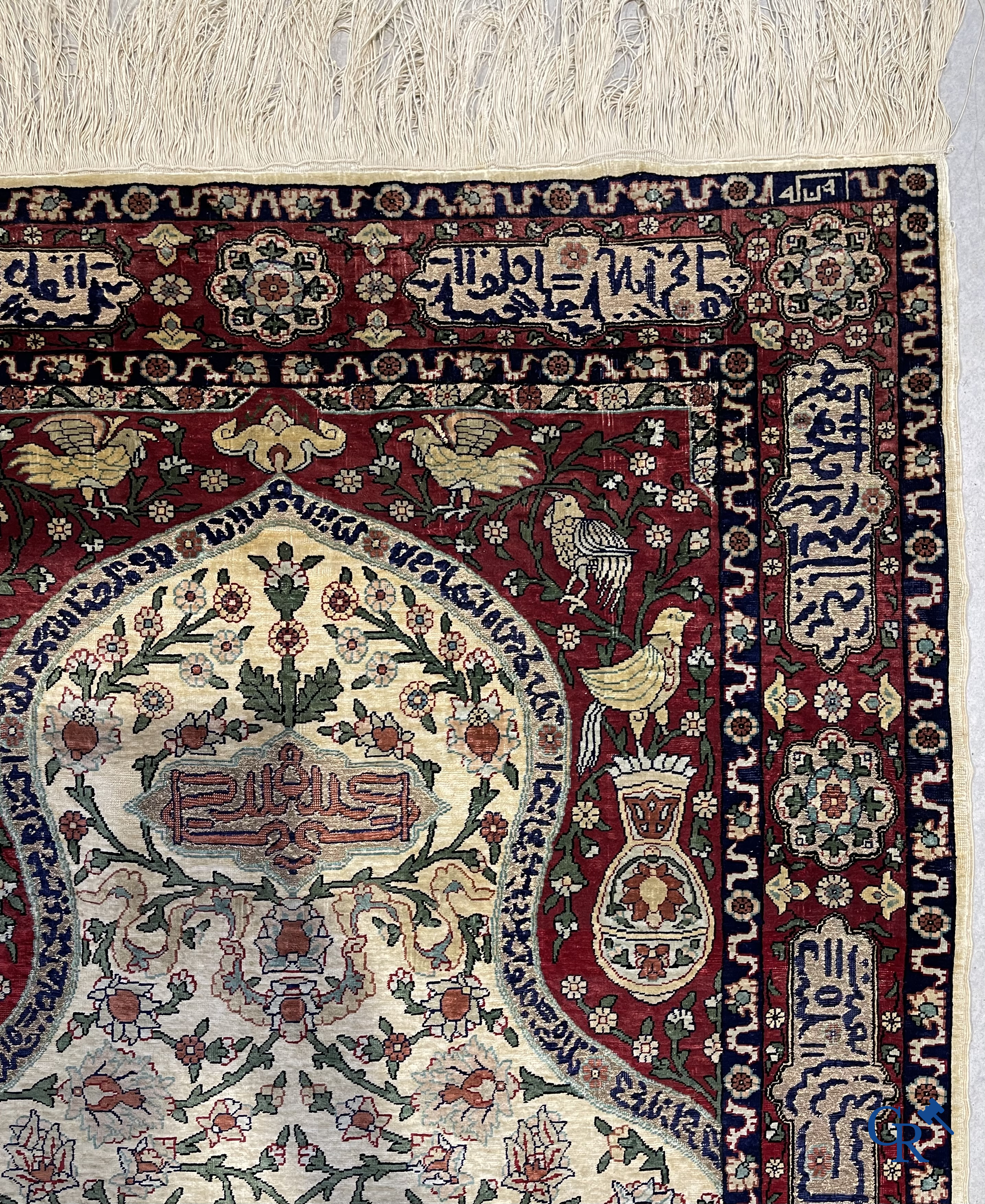 Oosterse tapijten. Een zijden gesigneerd tapijt op donkerrode achtergrond. Inscripties en bewerkt met gouddraad.