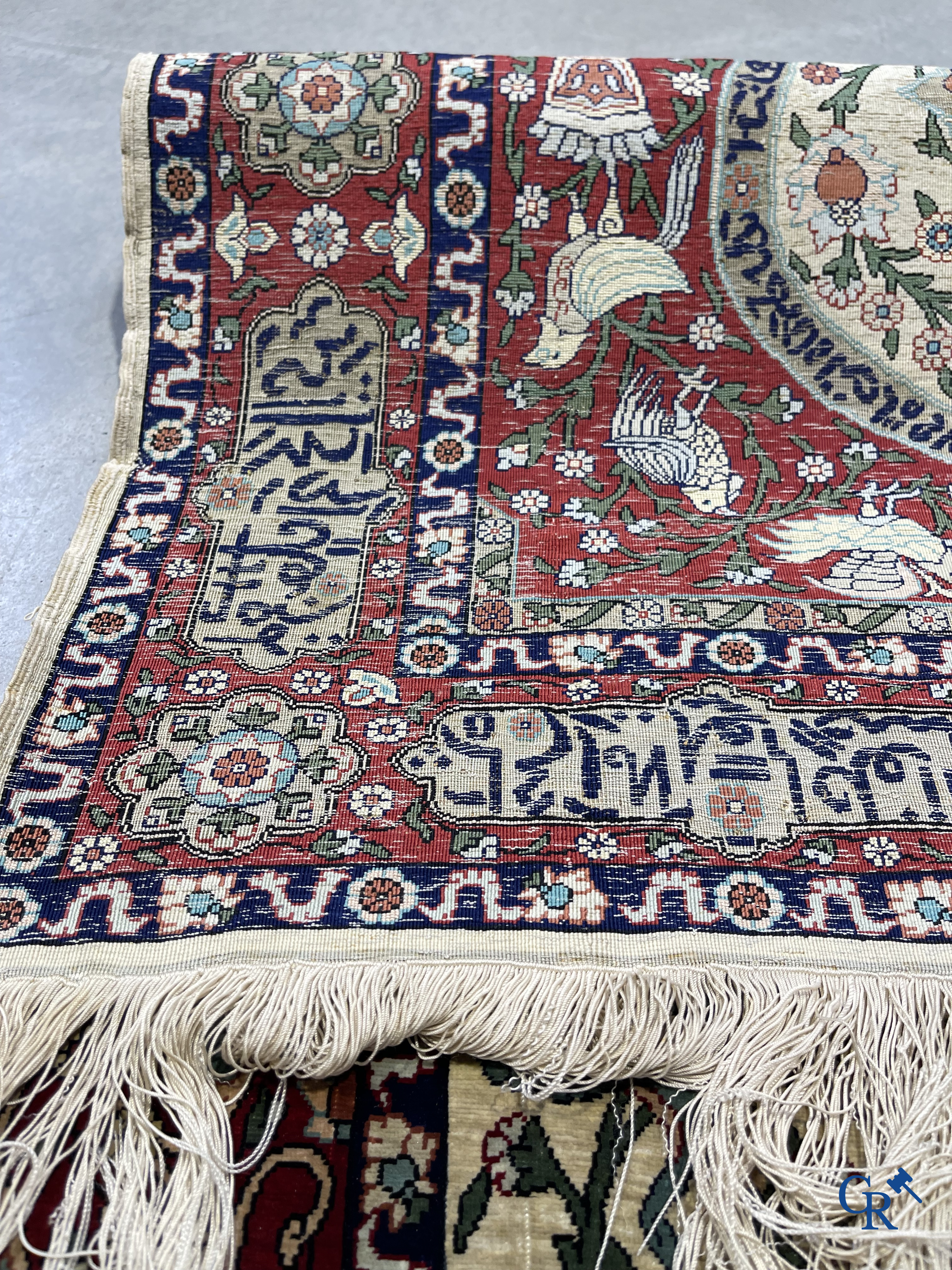 Oosterse tapijten. Een zijden gesigneerd tapijt op donkerrode achtergrond. Inscripties en bewerkt met gouddraad.