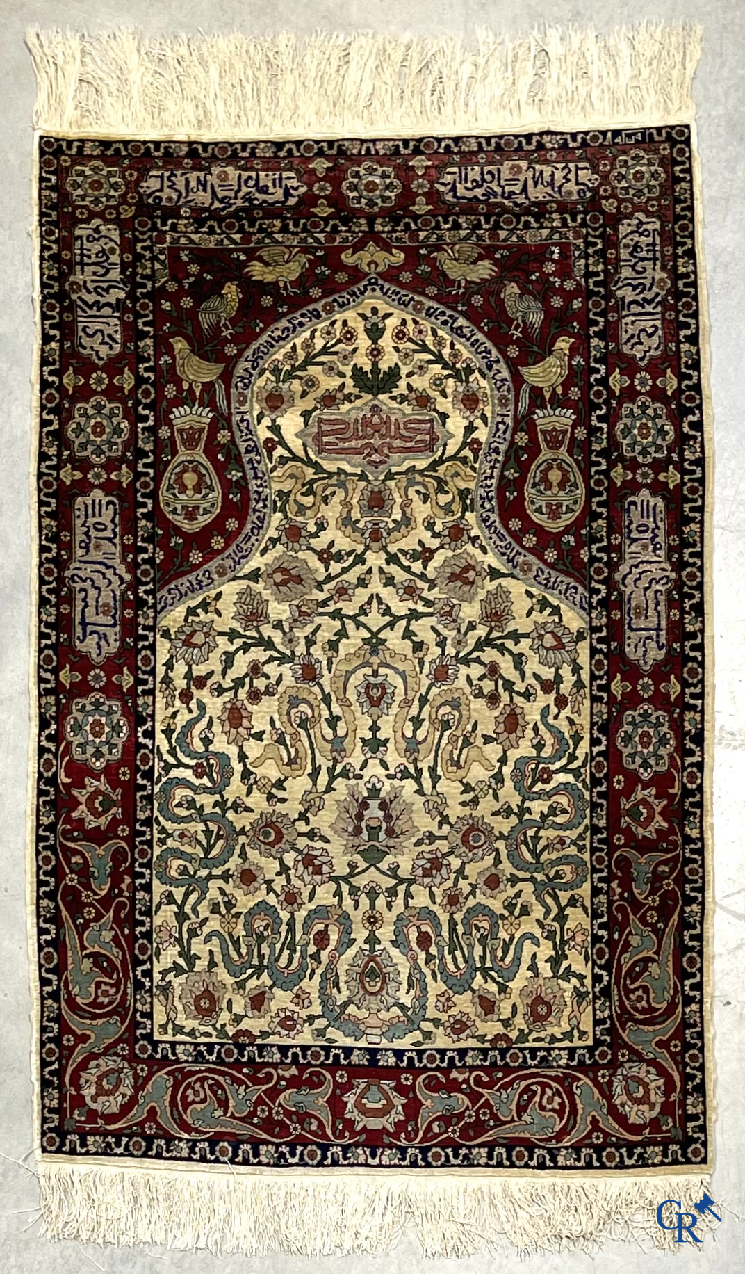 Oosterse tapijten. Een zijden gesigneerd tapijt op donkerrode achtergrond. Inscripties en bewerkt met gouddraad.