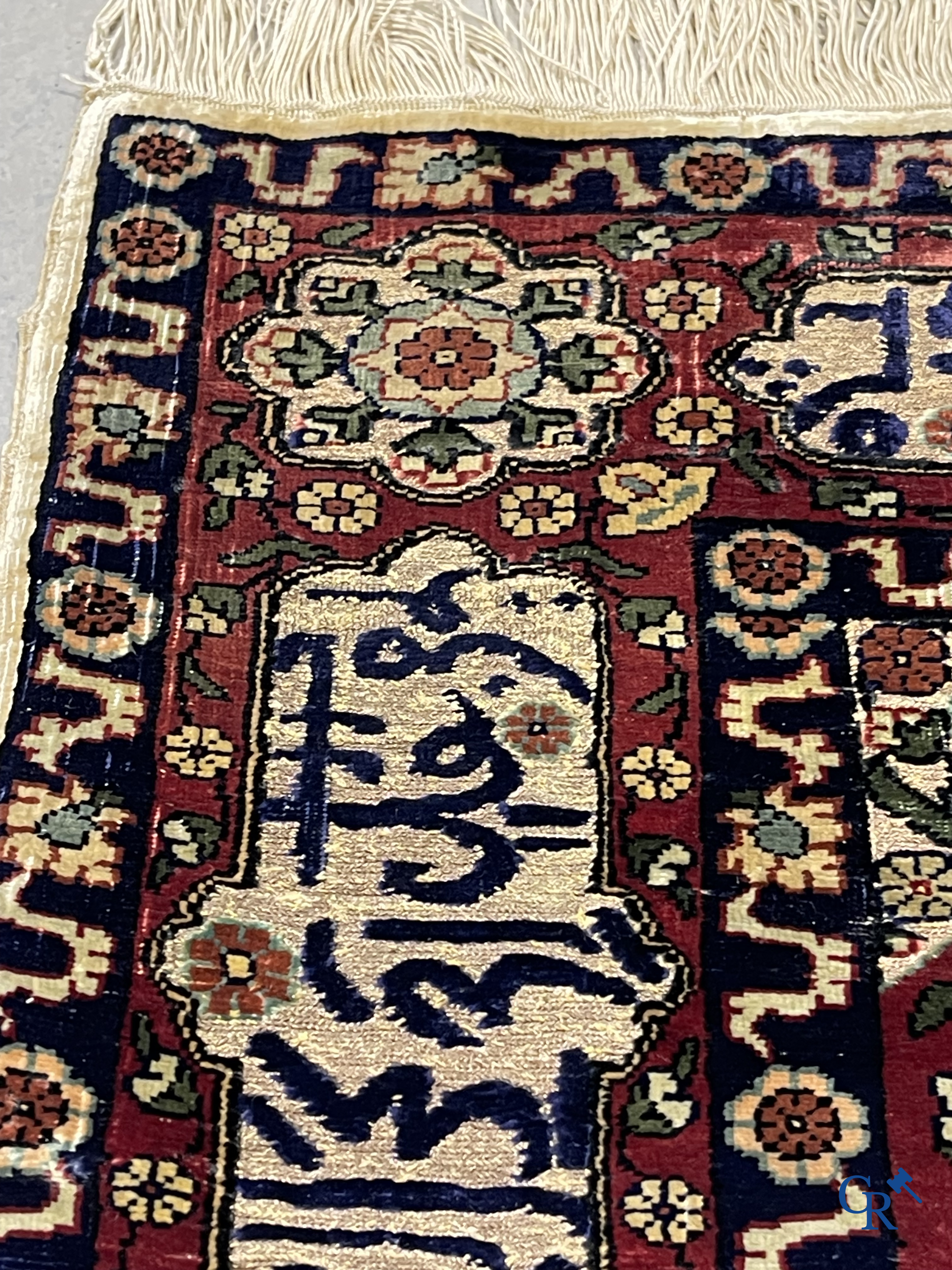 Oosterse tapijten. Een zijden gesigneerd tapijt op donkerrode achtergrond. Inscripties en bewerkt met gouddraad.