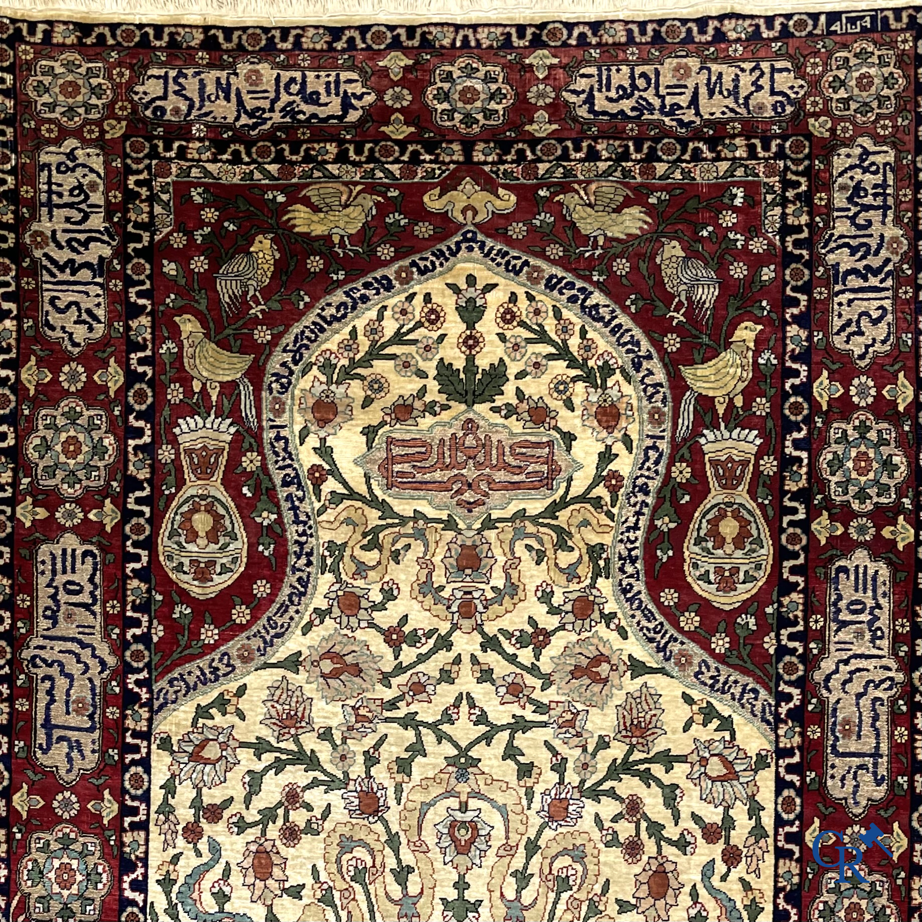 Oosterse tapijten. Een zijden gesigneerd tapijt op donkerrode achtergrond. Inscripties en bewerkt met gouddraad.