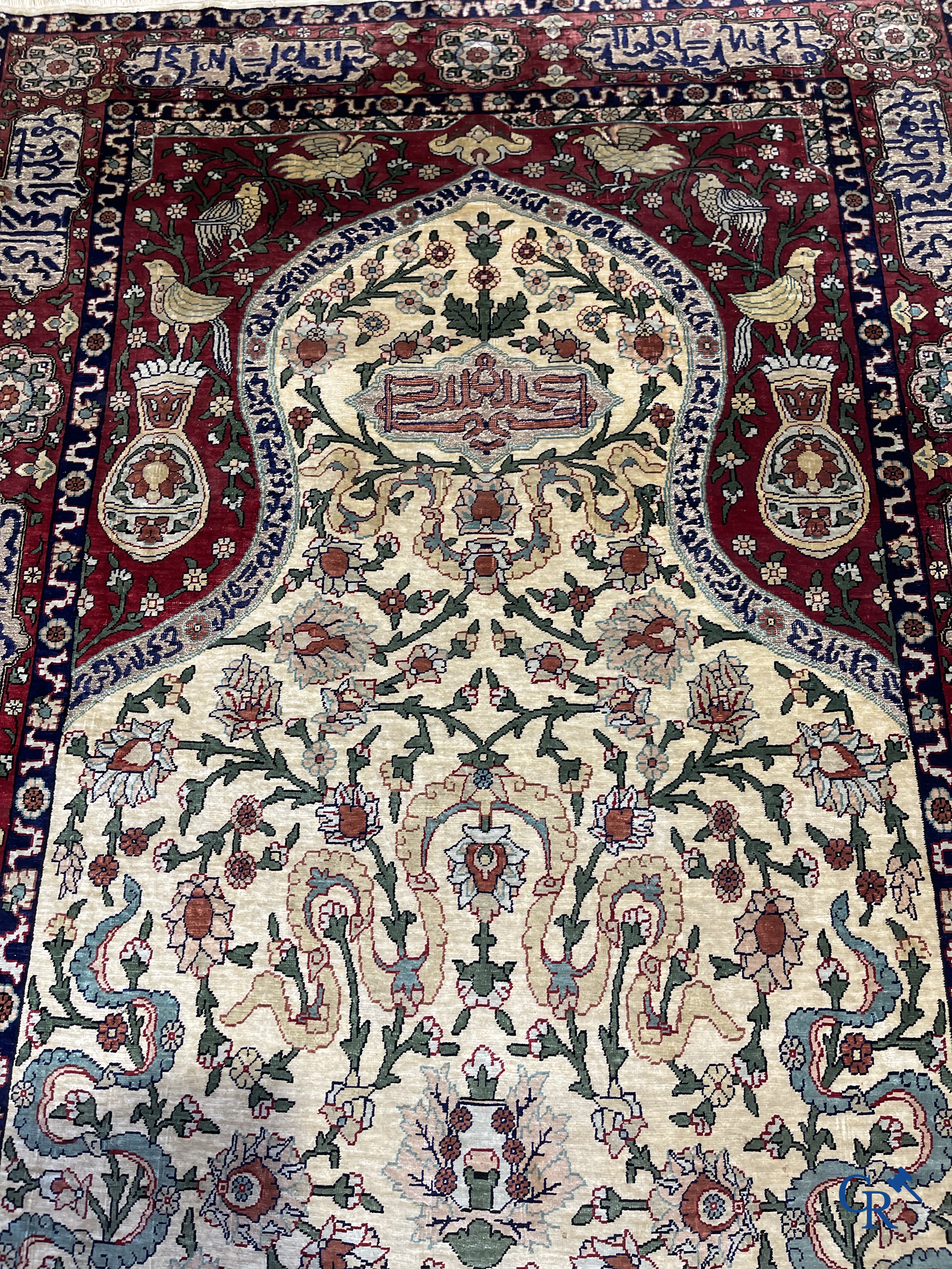 Oosterse tapijten. Een zijden gesigneerd tapijt op donkerrode achtergrond. Inscripties en bewerkt met gouddraad.