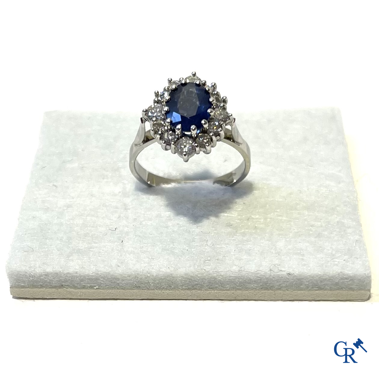 Jewellery. Ring in white gold 750°/00 set with a central blue sapphire surrounded by 12 small diamonds.