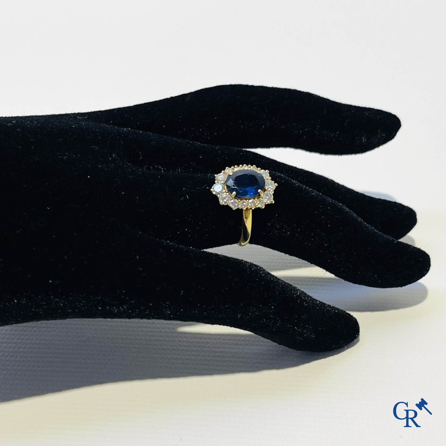 Juwelen. Ring in geelgoud 750°/00 bezet met een centrale blauwe saffier omringd door 14 kleine diamanten.