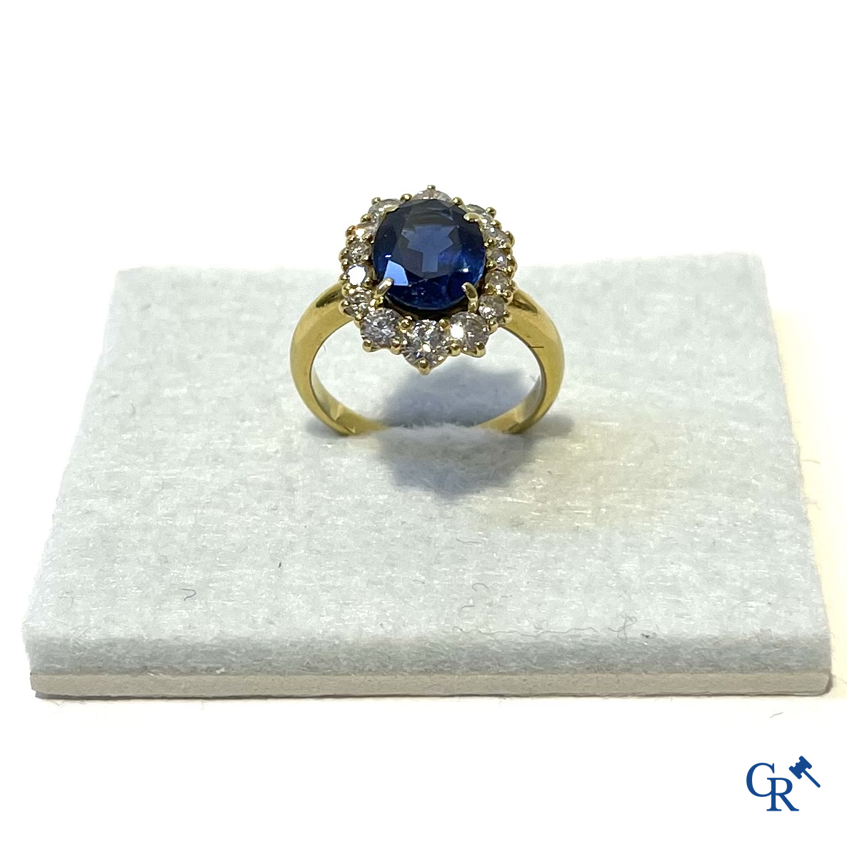 Juwelen. Ring in geelgoud 750°/00 bezet met een centrale blauwe saffier omringd door 14 kleine diamanten.
