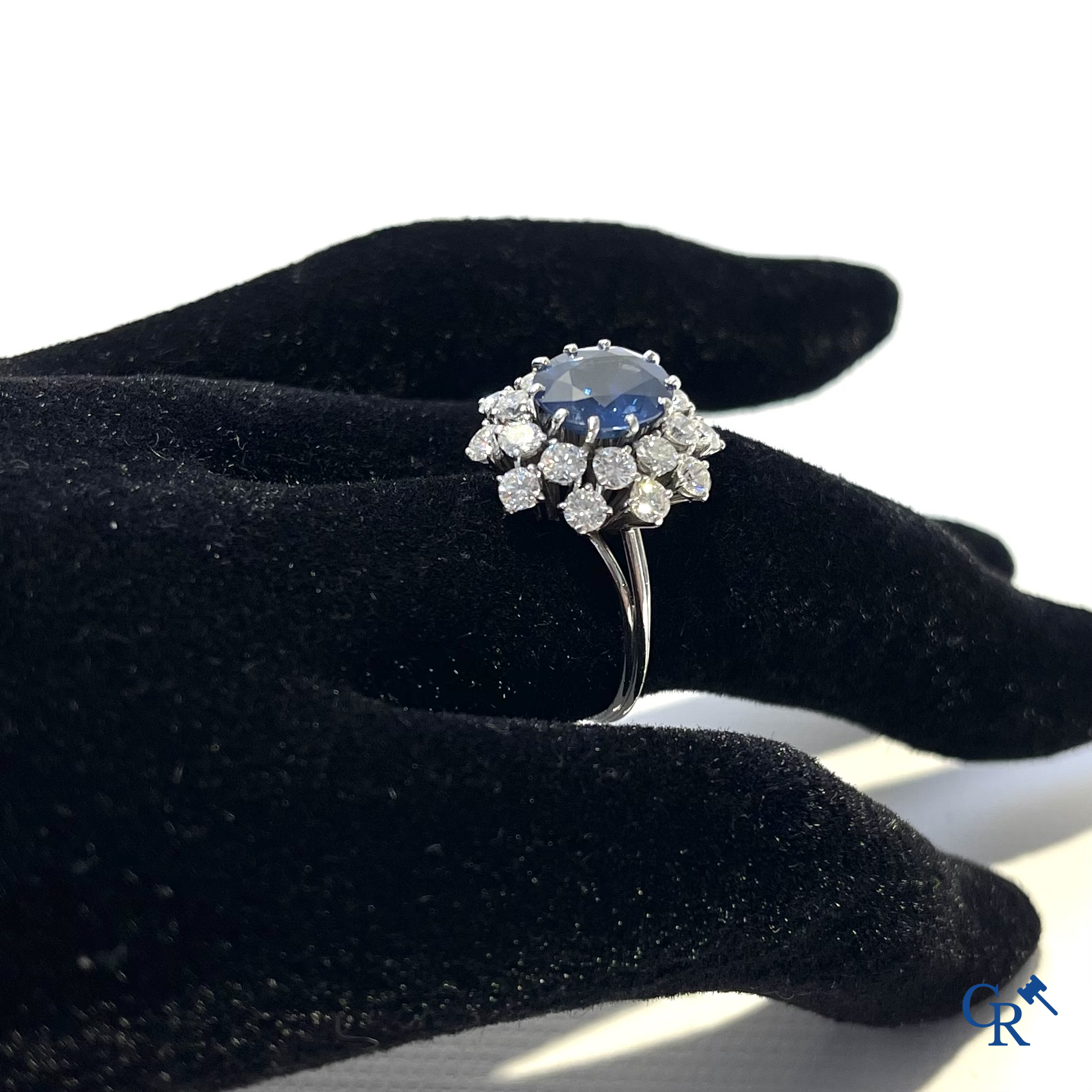 Juwelen. Ring in witgoud 750°/00 bezet met een centrale blauwe saffier omringd door 20 kleine diamanten.