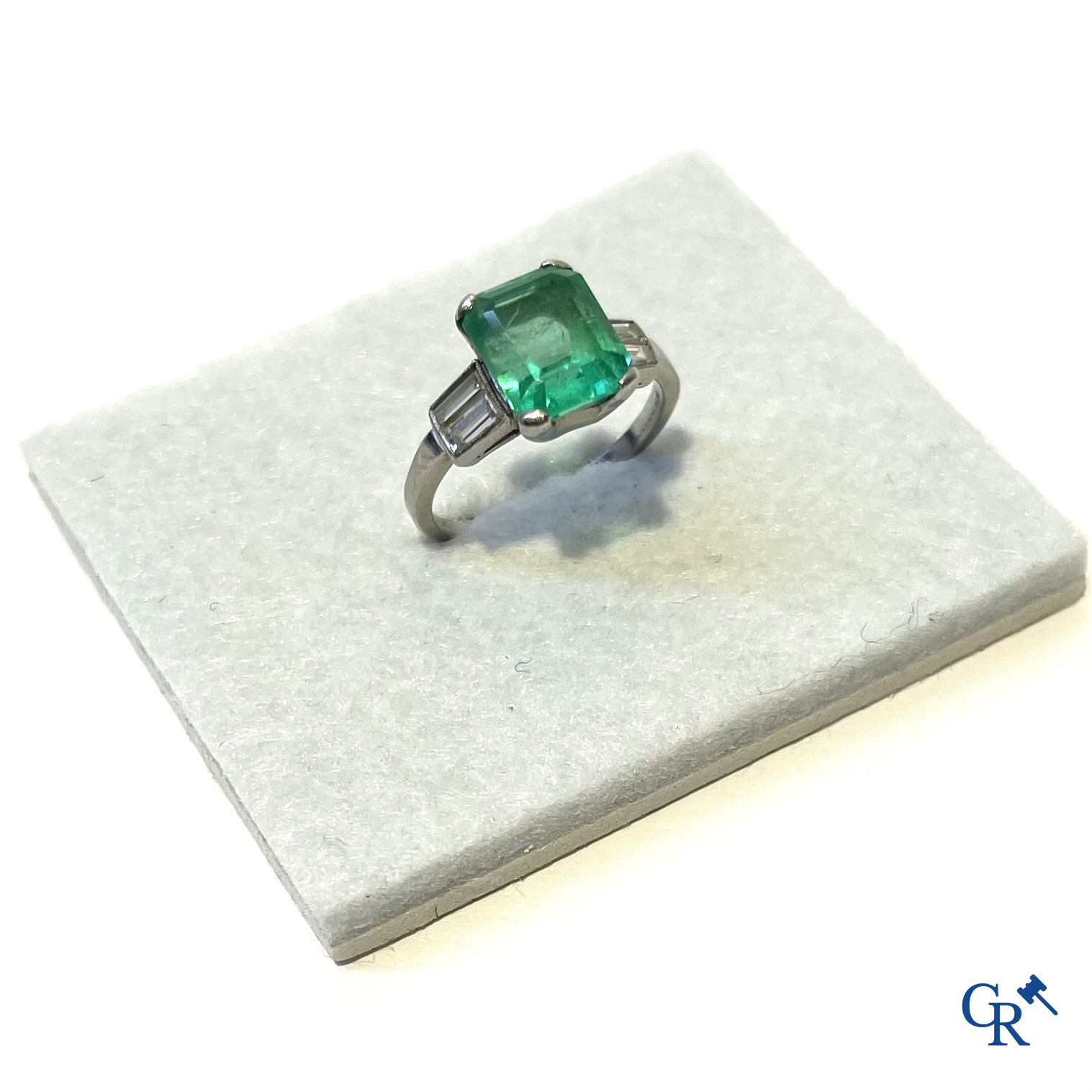 Juwelen. Een platina ring met smaragd en diamanten en een hanger in witgoud 750°/00 met smaragd en 14 diamanten.