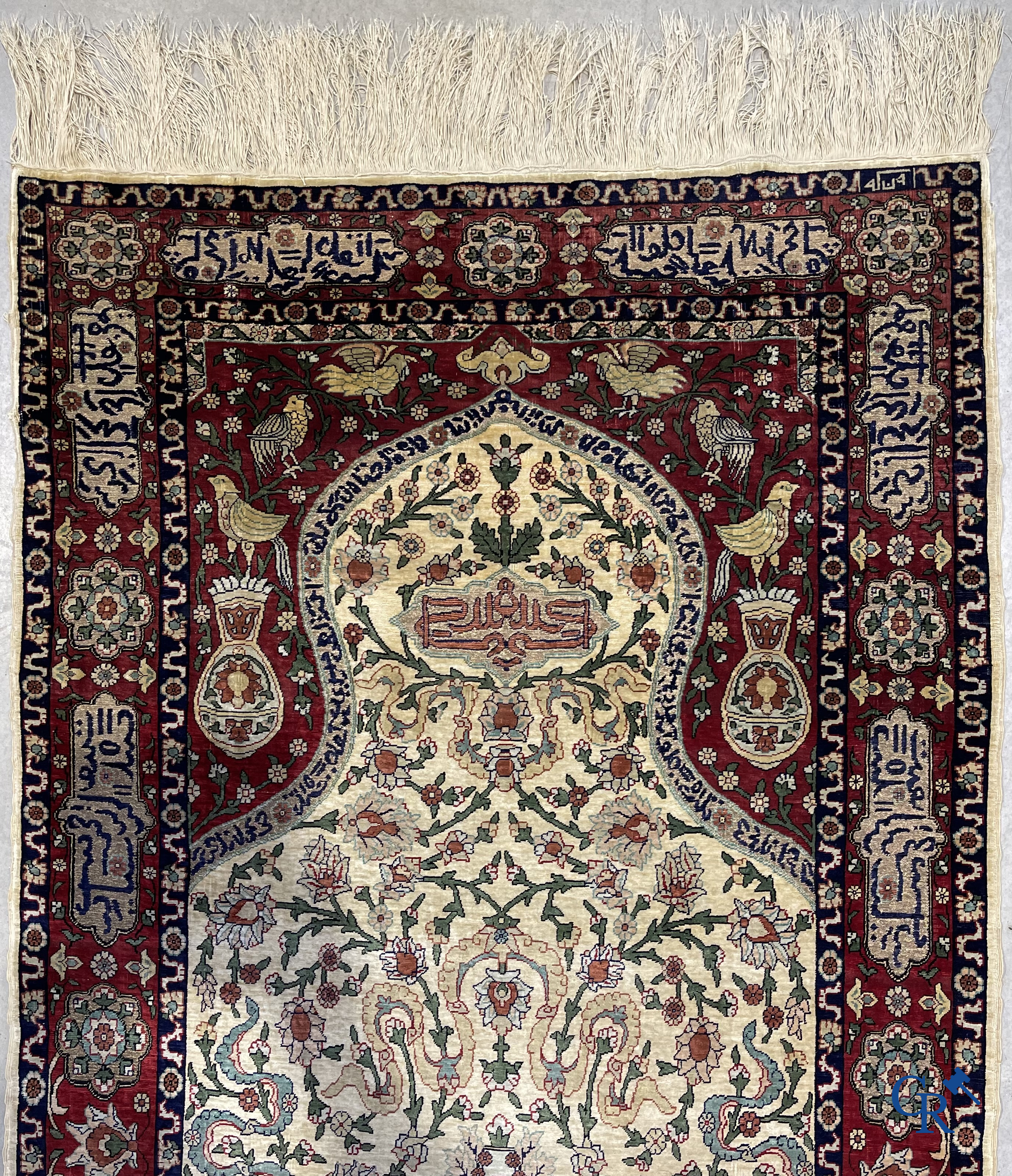 Oosterse tapijten. Een zijden gesigneerd tapijt op donkerrode achtergrond. Inscripties en bewerkt met gouddraad.