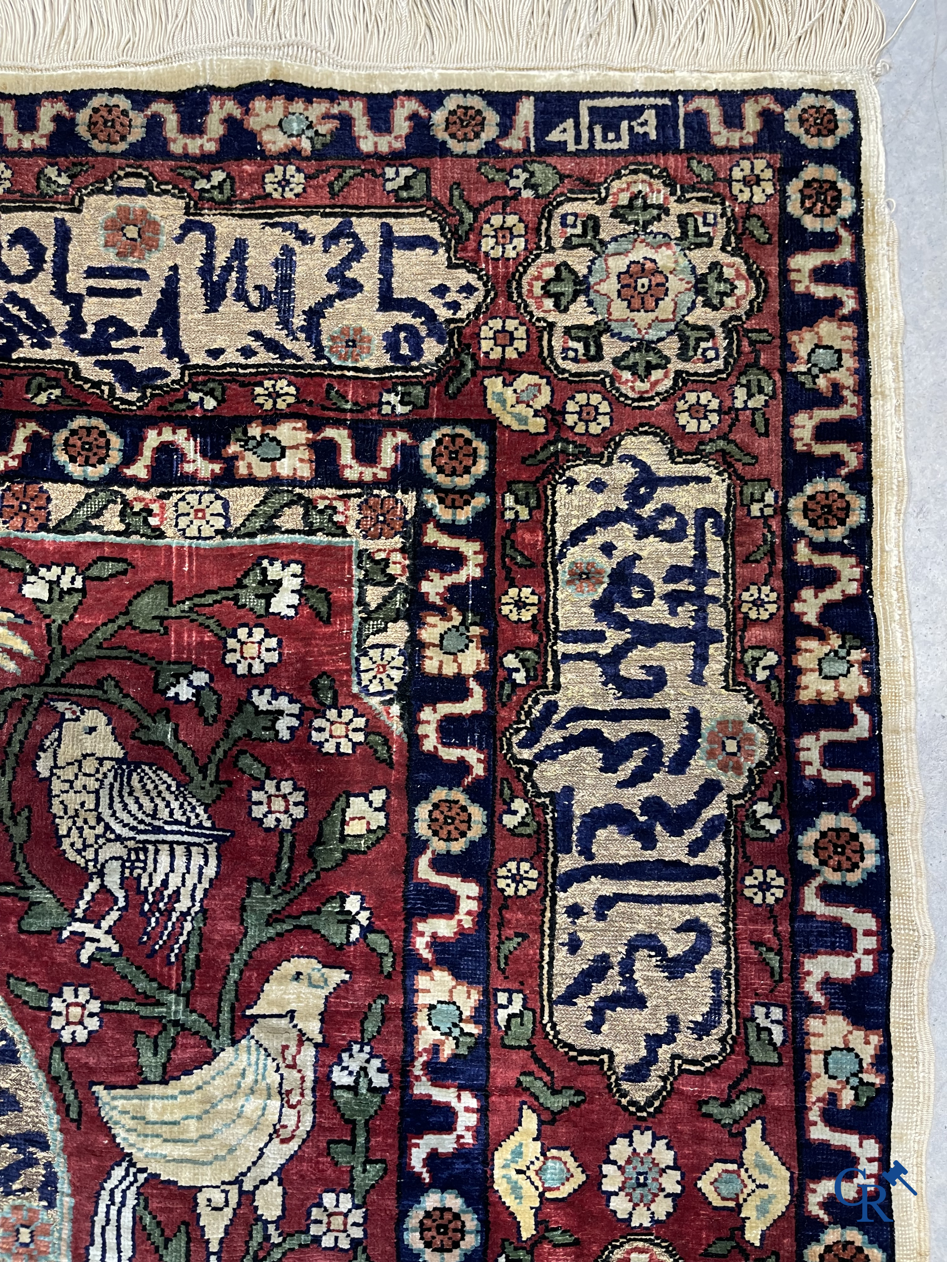 Oosterse tapijten. Een zijden gesigneerd tapijt op donkerrode achtergrond. Inscripties en bewerkt met gouddraad.