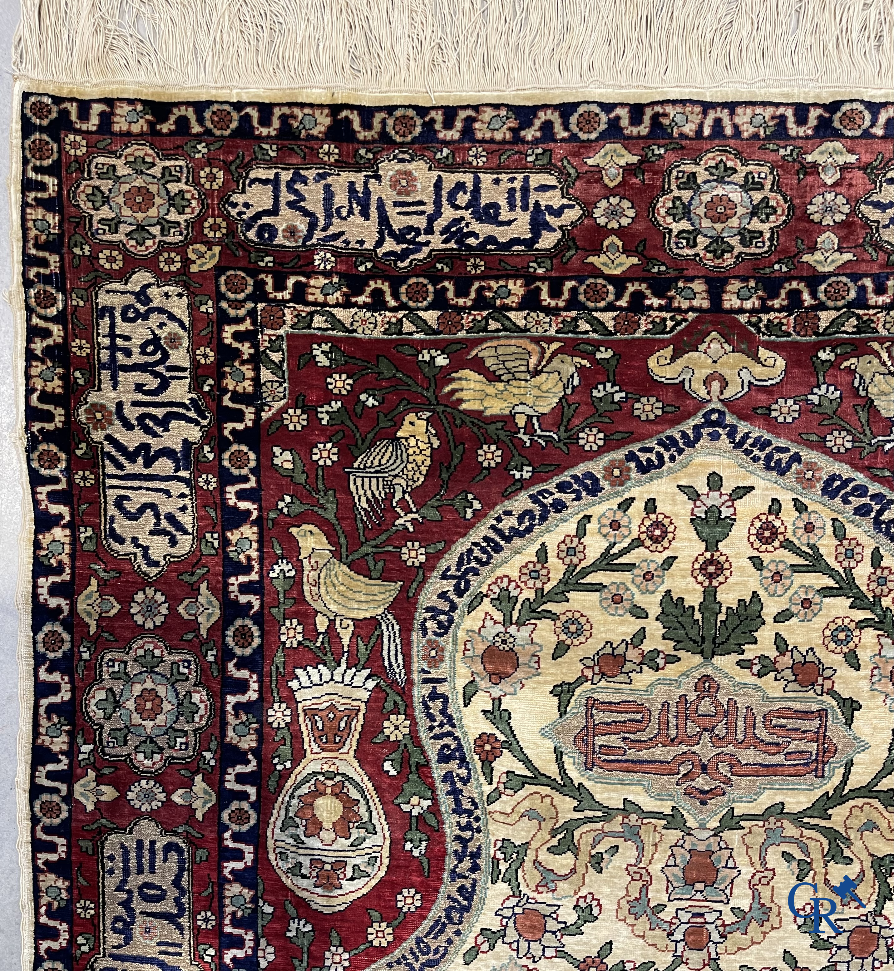 Oosterse tapijten. Een zijden gesigneerd tapijt op donkerrode achtergrond. Inscripties en bewerkt met gouddraad.