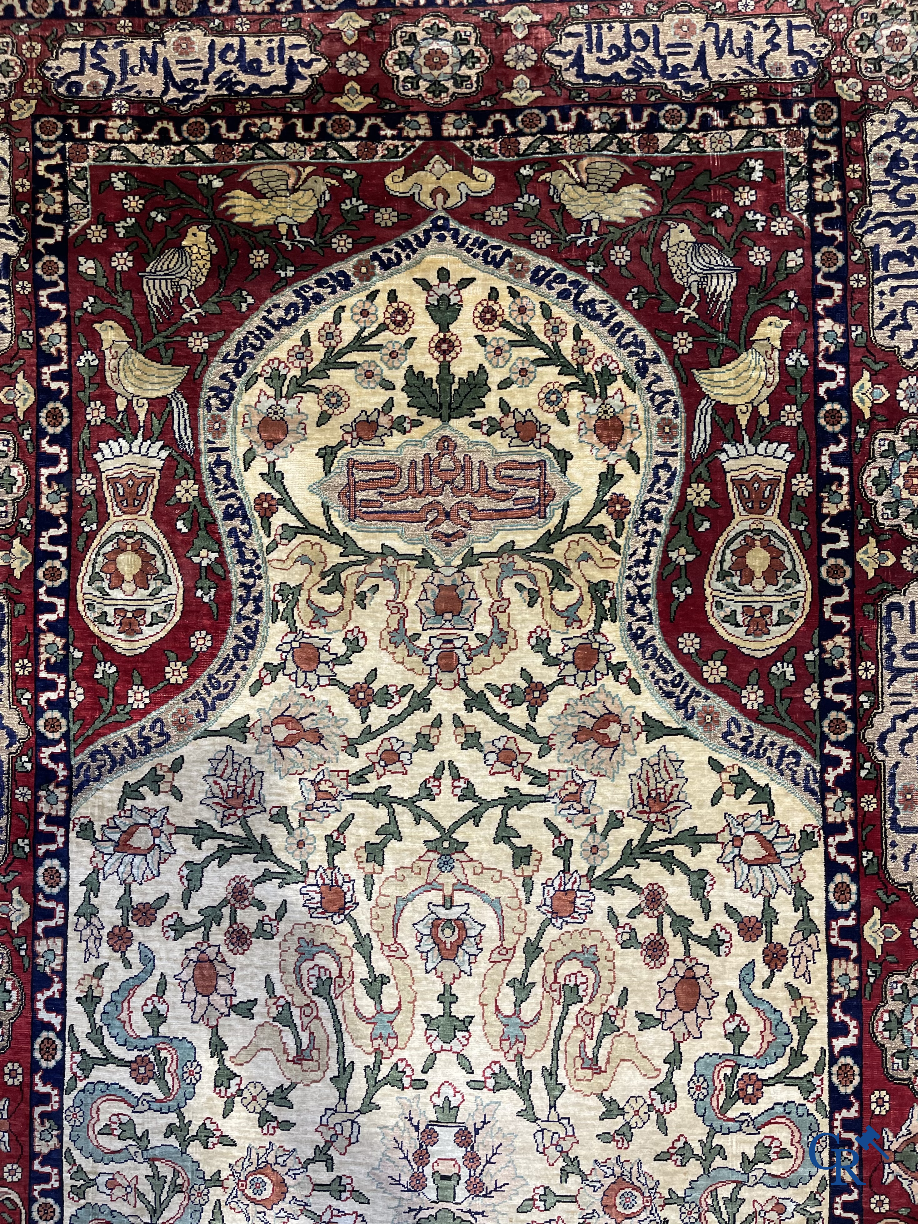 Oosterse tapijten. Een zijden gesigneerd tapijt op donkerrode achtergrond. Inscripties en bewerkt met gouddraad.